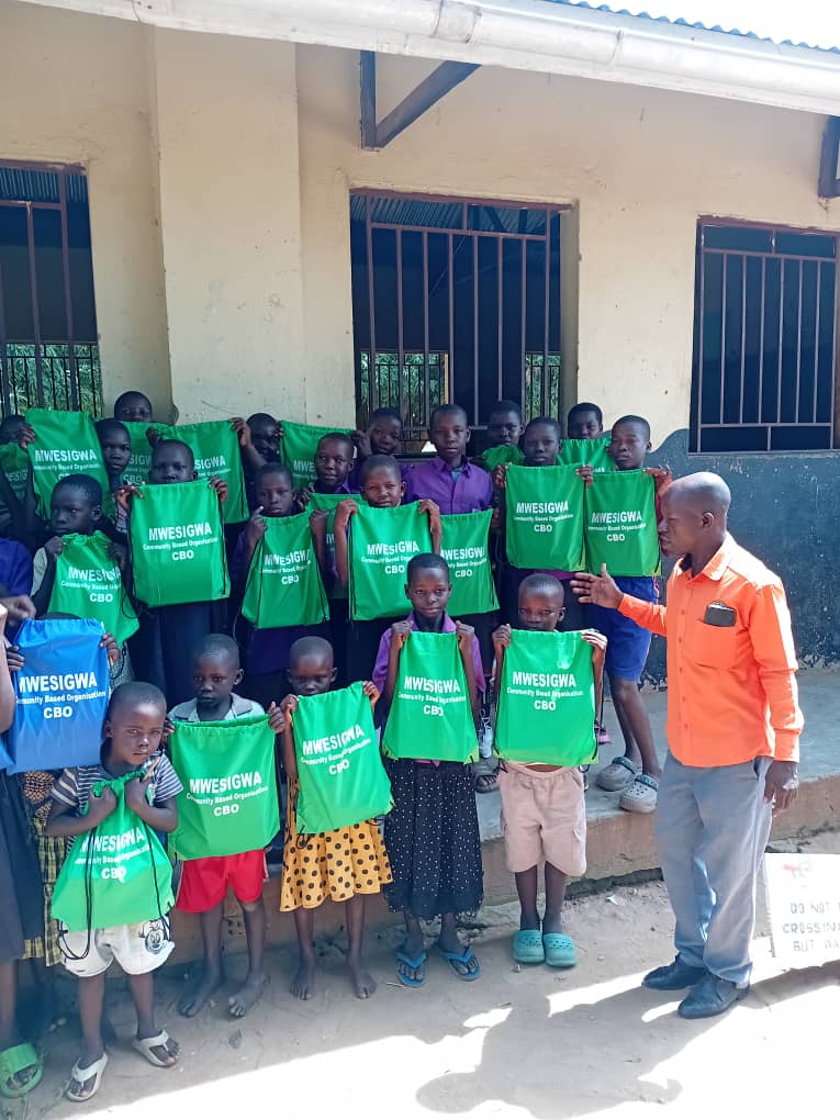 Children presenting green Mwesigwa CBO learner-support bags during school outreach