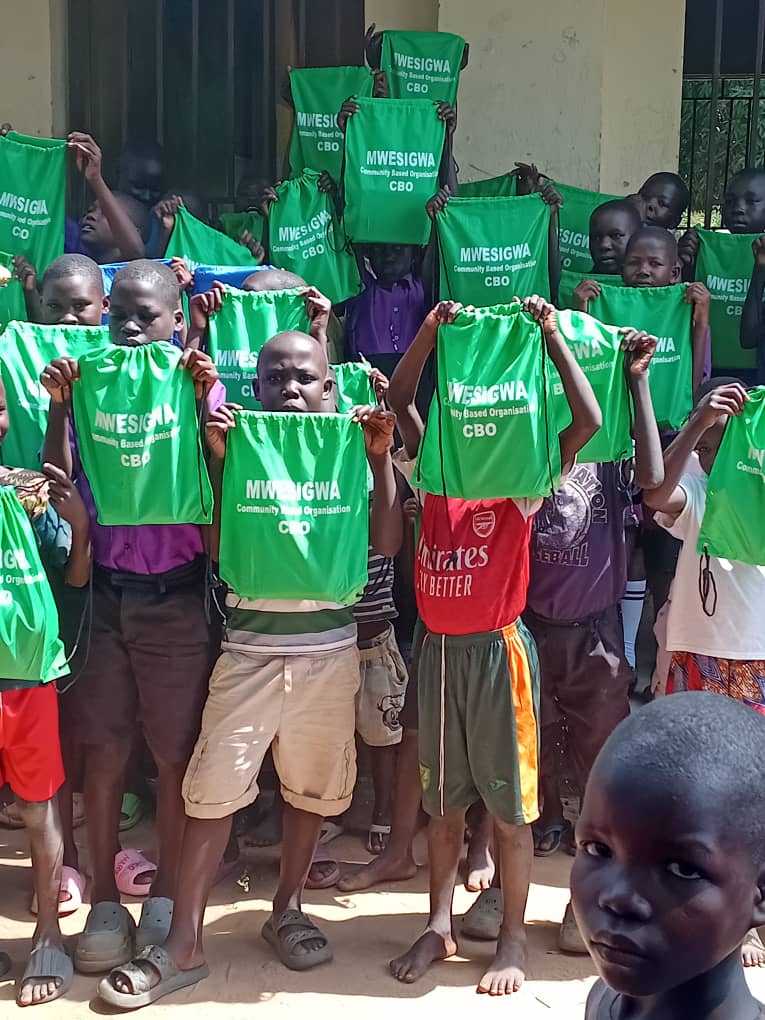 Children presenting Mwesigwa CBO learner-support bags during outreach